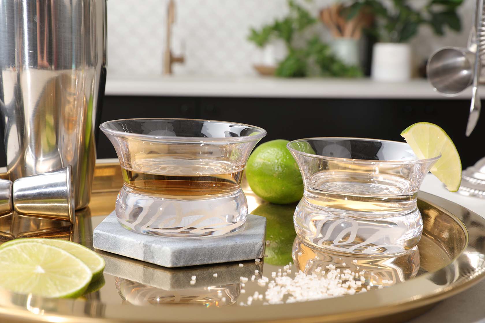 Close up of two Oaxaca glasses on a bronze tray, decorated with cut limes and salt.