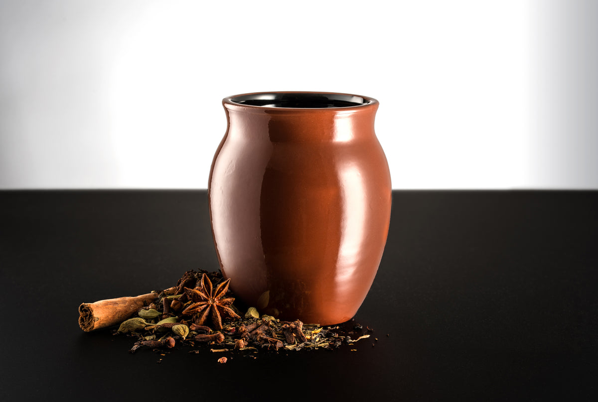 A glossy finish Jalisco jug on a black countertop and white background. Surrounded by spices consisting of cinnamon sticks, star anise, and other spices.