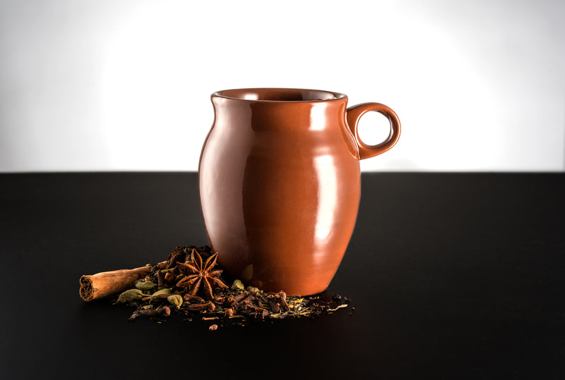 A glossy finish Jalisco jug with handle on a black countertop and white background. Surrounded by spices consisting of cinnamon sticks, star anise, and other spices.