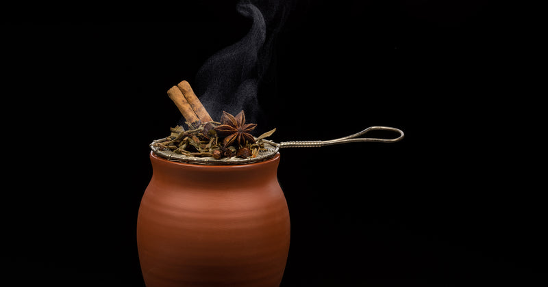 A matte finish Jalisco jug on a black background. The jug is covered on top by an antique tea strainer filled with spices consisting of cinnamon sticks, star anise, and other spices.