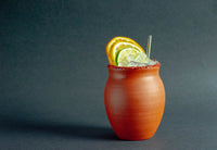 A matte finish Jalisco jug on a gray background, rimmed with red salt, and filled with small ice cubes and cut citrus.