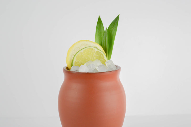 A matte finish Jalisco jug on a white background filled with small ice cubes, citrus slices, and pineapple leaves.