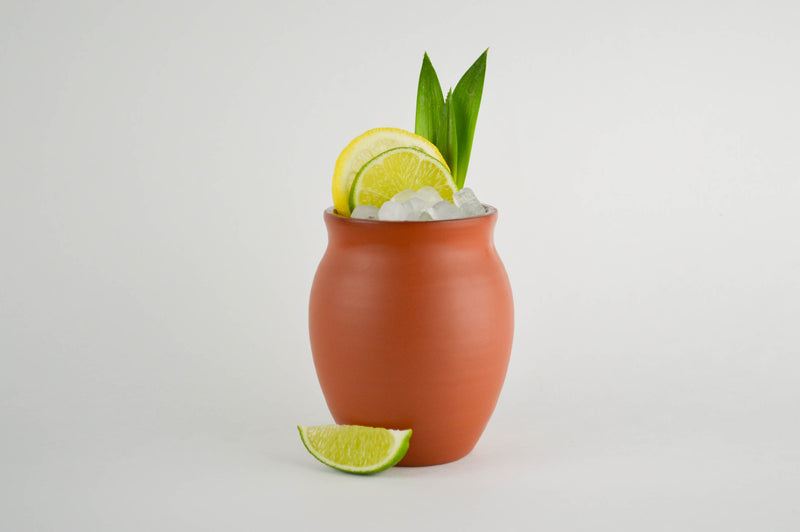 A matte finish Jalisco jug on a white background filled with small ice cubes, citrus slices, and pineapple leaves.