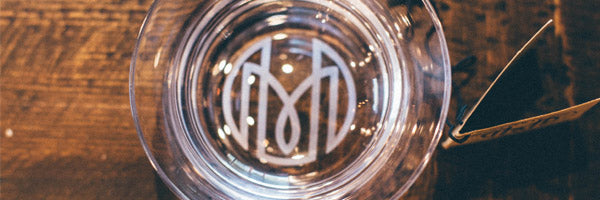 A close up overhead shot of the Oaxaca glass showing the Historically Modern monogram. The glass is sitting on a dark wood table.
