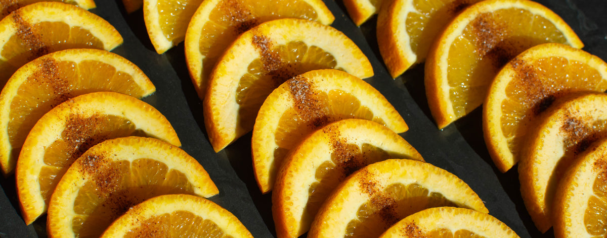 Three vertical rows of orange slices on a gray tray. Each row has a slim line of red salt over the oranges.