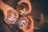 Three Oaxaca glasses cheers-ing, filled with different types of tequila and ice cubes.