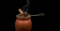 A matte finish Jalisco jug on a black background. The jug is covered on top by an antique tea strainer filled with spices consisting of cinnamon sticks, star anise, and other spices.